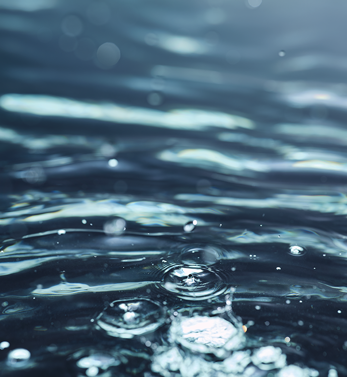 Close-up of rippling water with small bubbles and bright reflections on a dark blue surface.