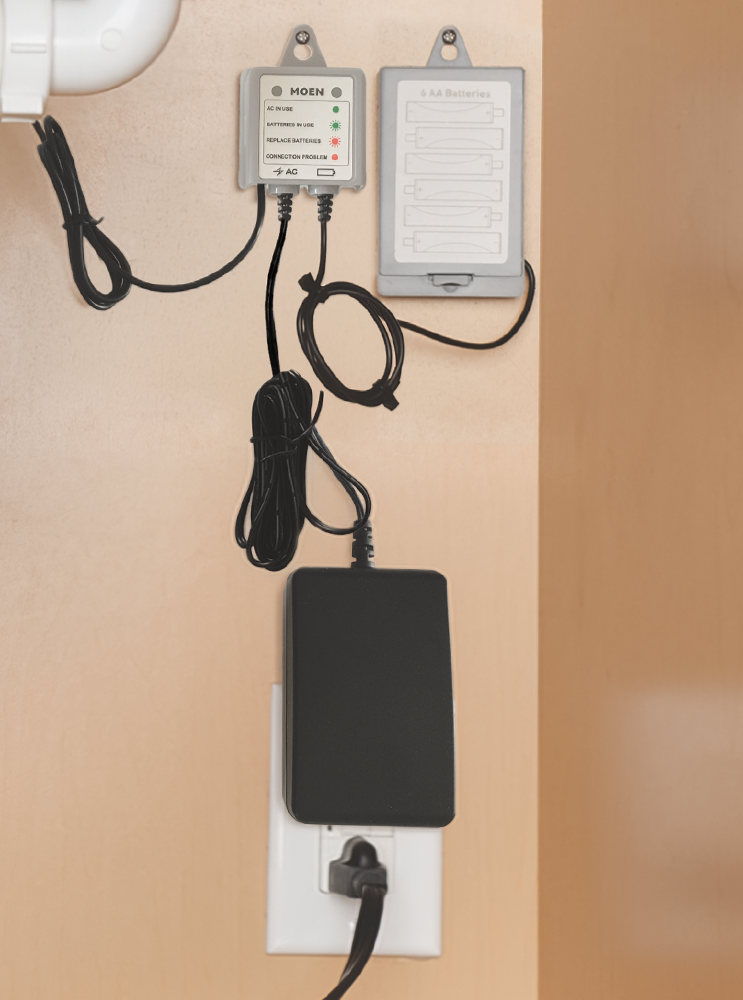 An AC adapter installed and plugged into a wall beneath a kitchen sink.