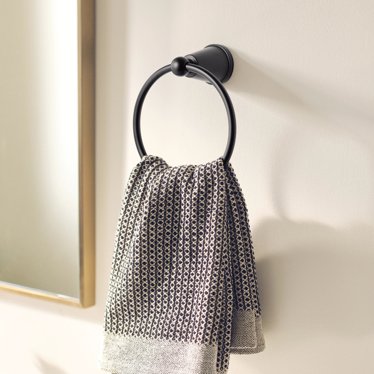 A black metal towel ring mounted on a beige wall, holding a textured black and white patterned hand towel.