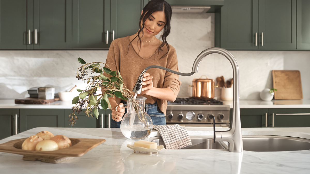 A woman using a Reflex retractable kitchen faucet to fill a vase.