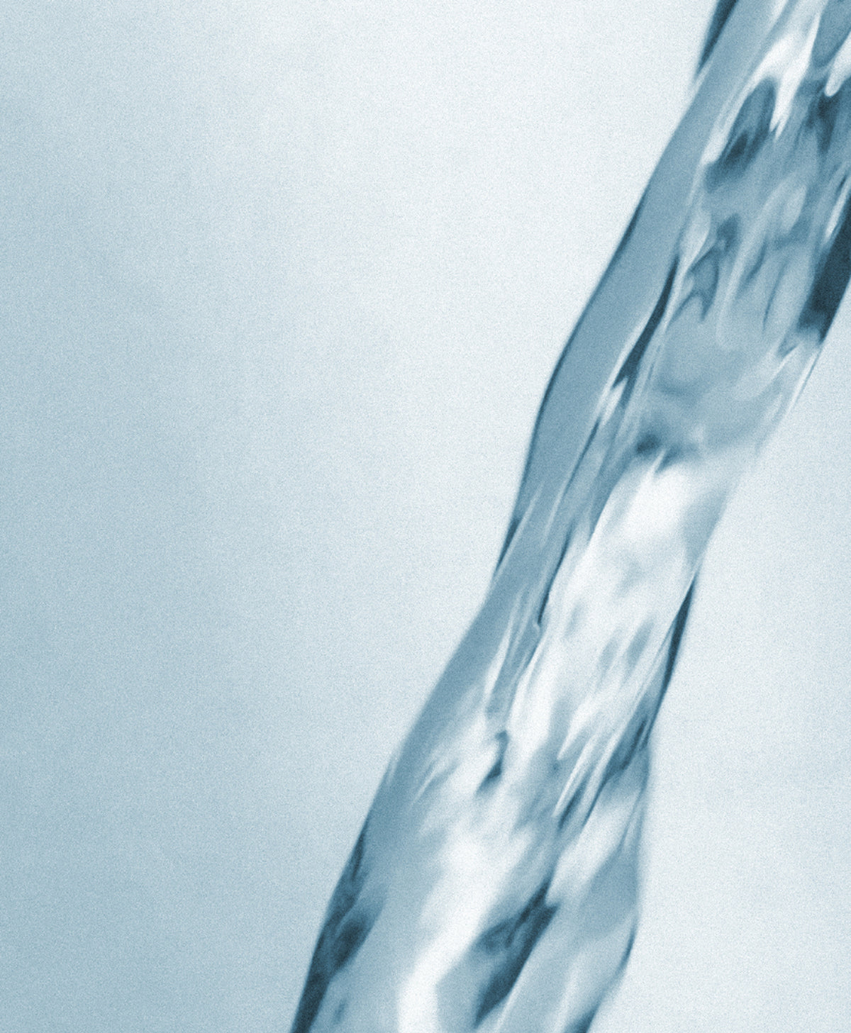 A close-up abstract shot of a clear, flowing stream of water against a pale blue-gray background.
