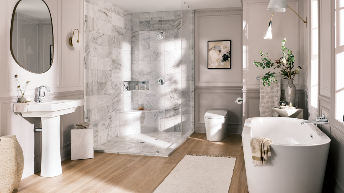 A luxury modern bathroom featuring a walk-in marble shower enclosure, a white pedestal sink, a freestanding white bathtub with a beige towel, light wood floors, and soft natural light.