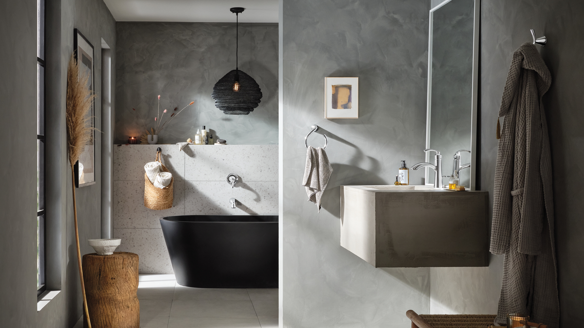 A split-view interior scene of a modern bathroom with textured gray walls, a black freestanding bathtub on the left and a floating white sink with chrome fixtures on the right, plus towels, a robe, pendant light, and framed wall art.