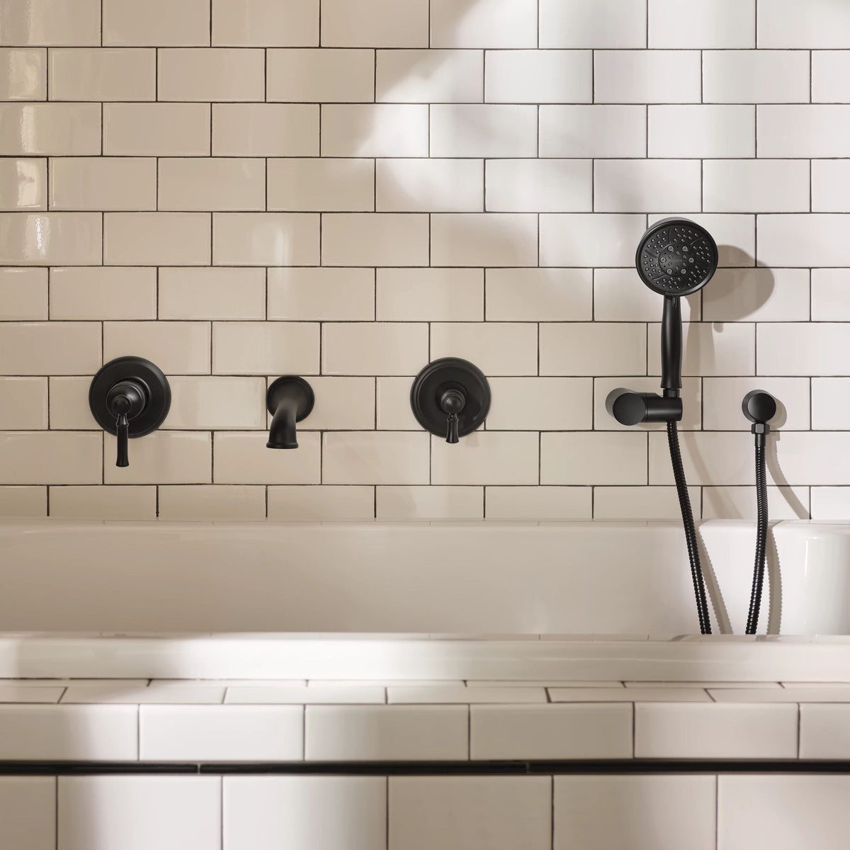Black matte bathroom faucet set with a handheld shower head mounted on a white subway-tiled wall above a bathtub.