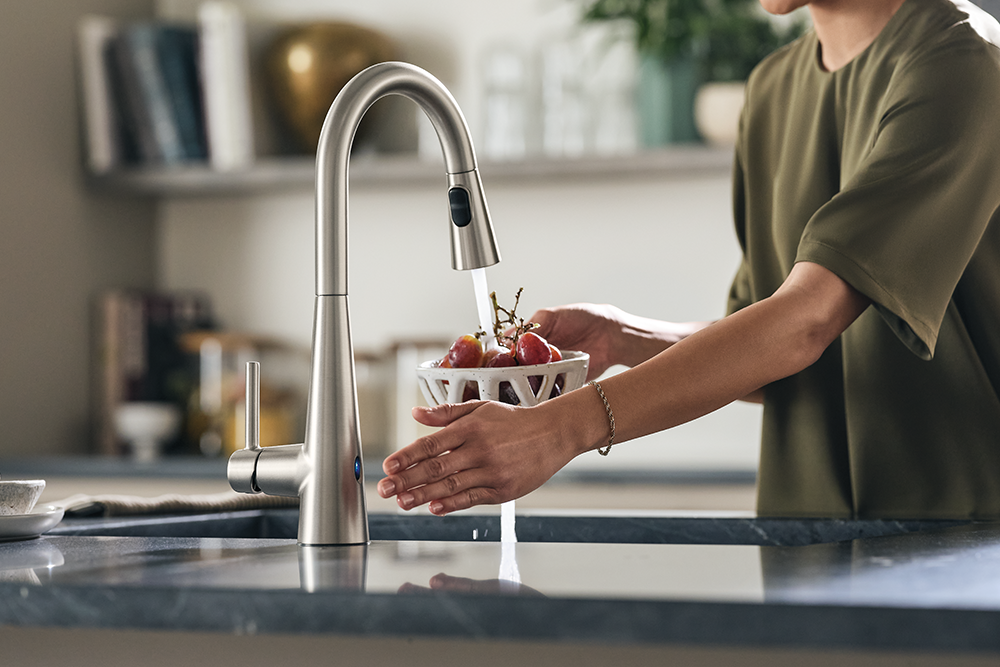 A woman turning a MotionSense Wave faucet on by waving her hand near the wave sensor.