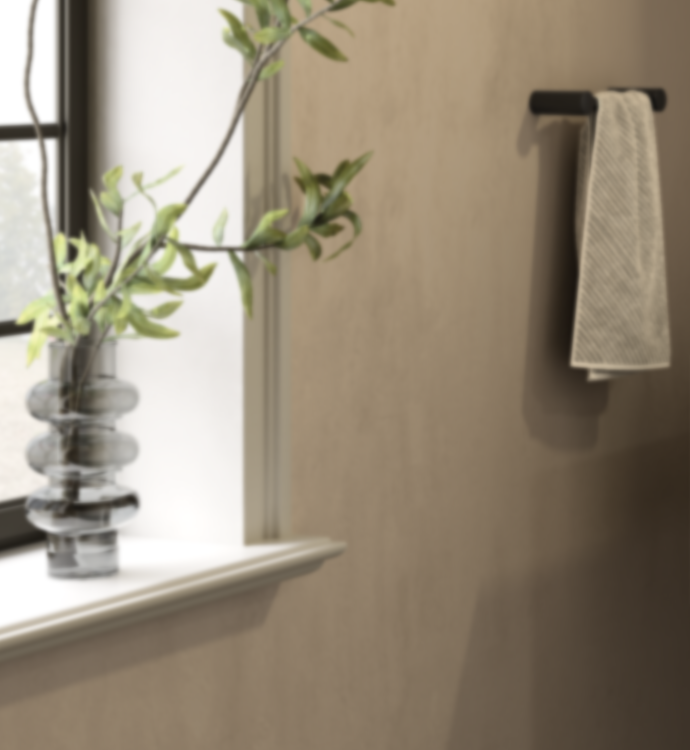 A beige textured wall with a black towel bar holding a cream towel, next to a window sill with a glass vase and green stems.