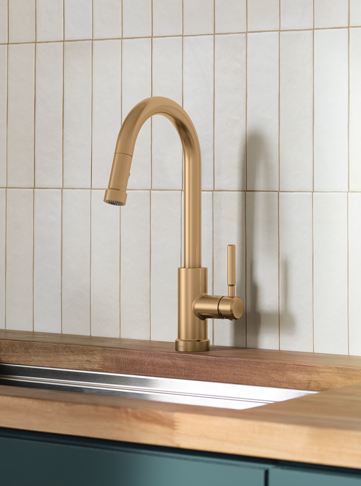 Kivo One-Handle High Arc Pulldown Kitchen Faucet in a brushed brass/gold finish, mounted on a wooden countertop with a stainless steel sink basin.