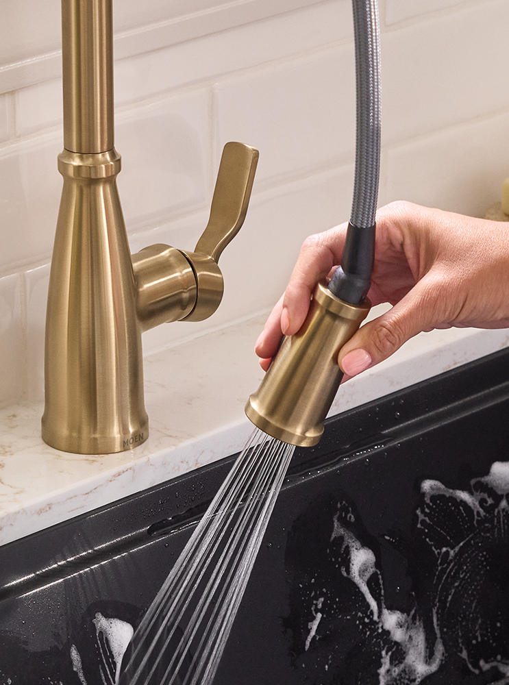 A hand holding a pulldown faucet sprayer to rinse a kitchen sink.