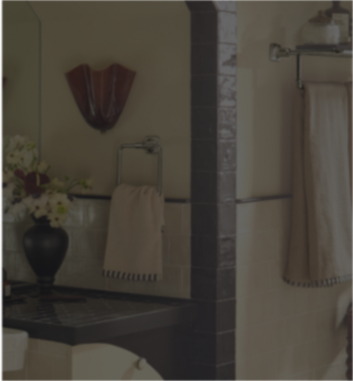 A beige cotton hand towel with black fringe trim hanging on a chrome wall-mounted towel ring in a bathroom setting.