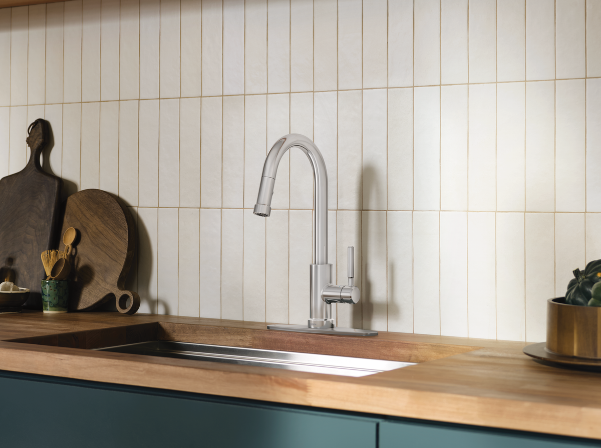 A modern single-handle kitchen faucet in polished silver stainless steel, installed on a wooden countertop with a matching tiled backsplash.