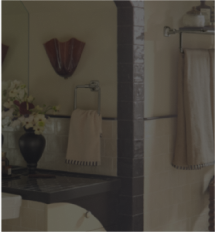 A beige cotton hand towel with black fringe trim hanging from a silver metal towel ring in a bathroom setting.