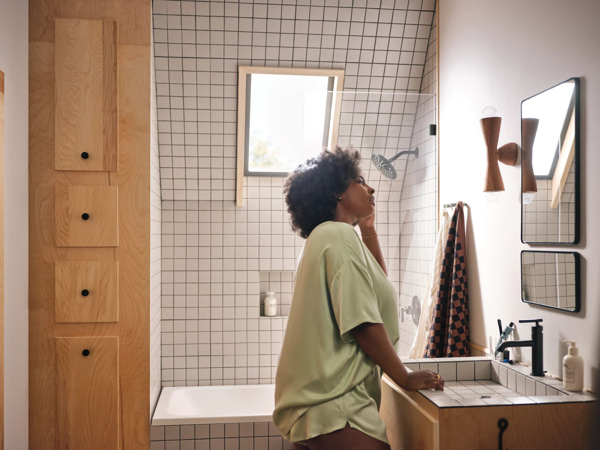 Woman standing in a bathroom looking at herself in the mirror.
