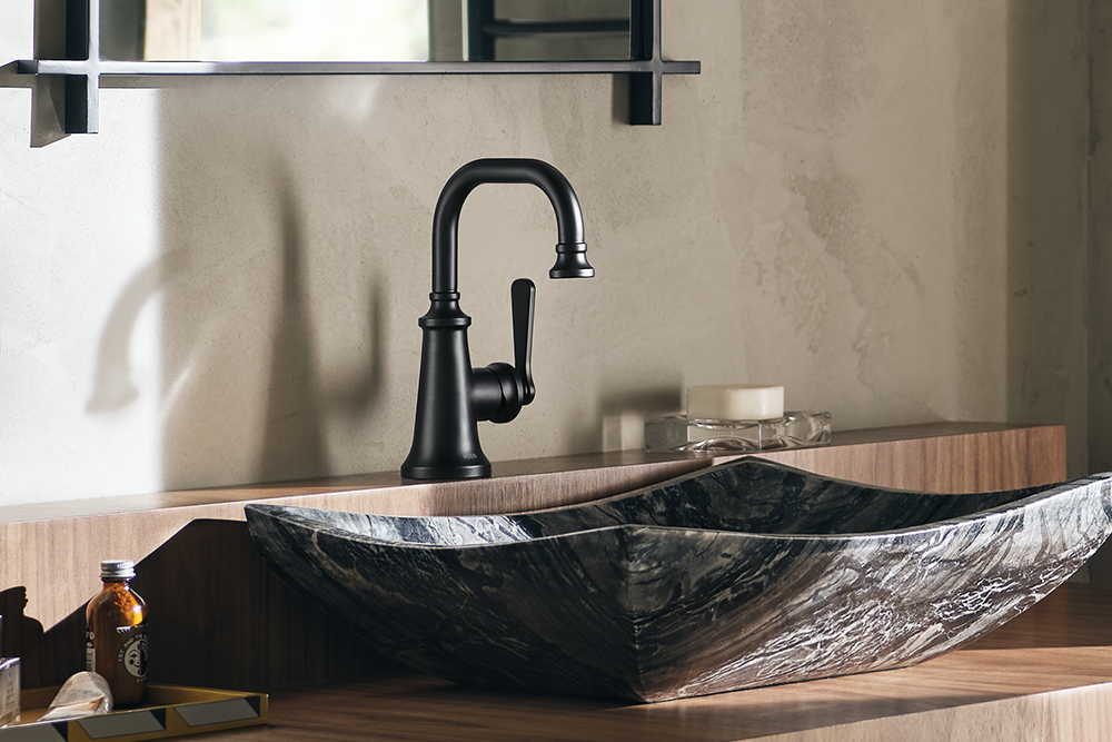 Colinet One-Handle High Arc Bathroom Faucet mounted above a dark marbled vessel sink on a wooden vanity against a textured beige wall.