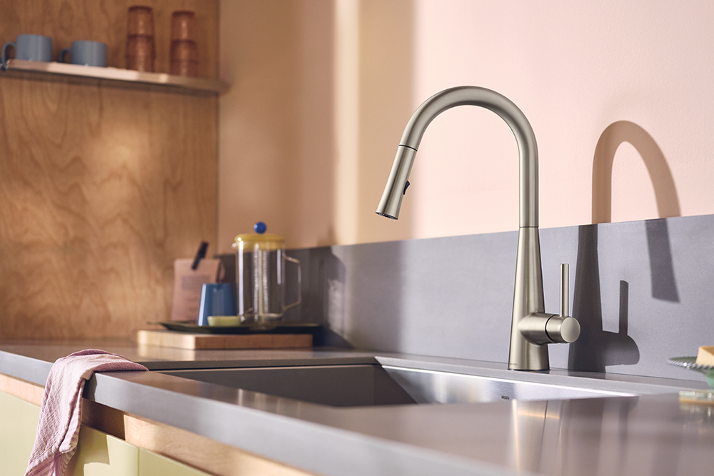 A modern matte gray pull-down kitchen faucet installed over a stainless steel sink in a warm-toned kitchen setting.