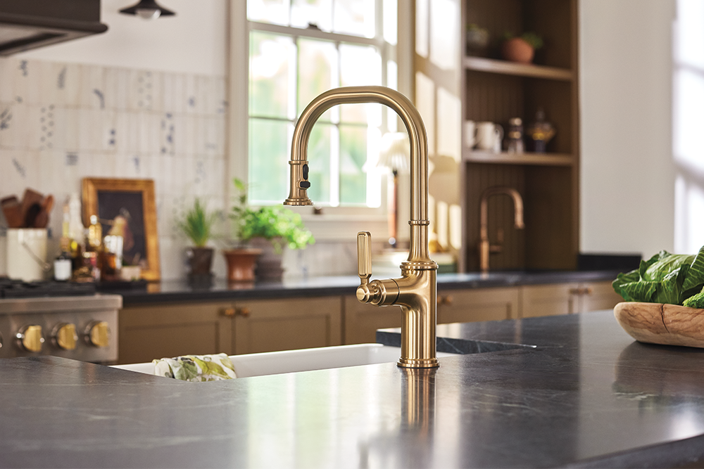 A polished brass kitchen faucet with a high-arc spout and lever handle, installed in a modern kitchen sink with a dark countertop.