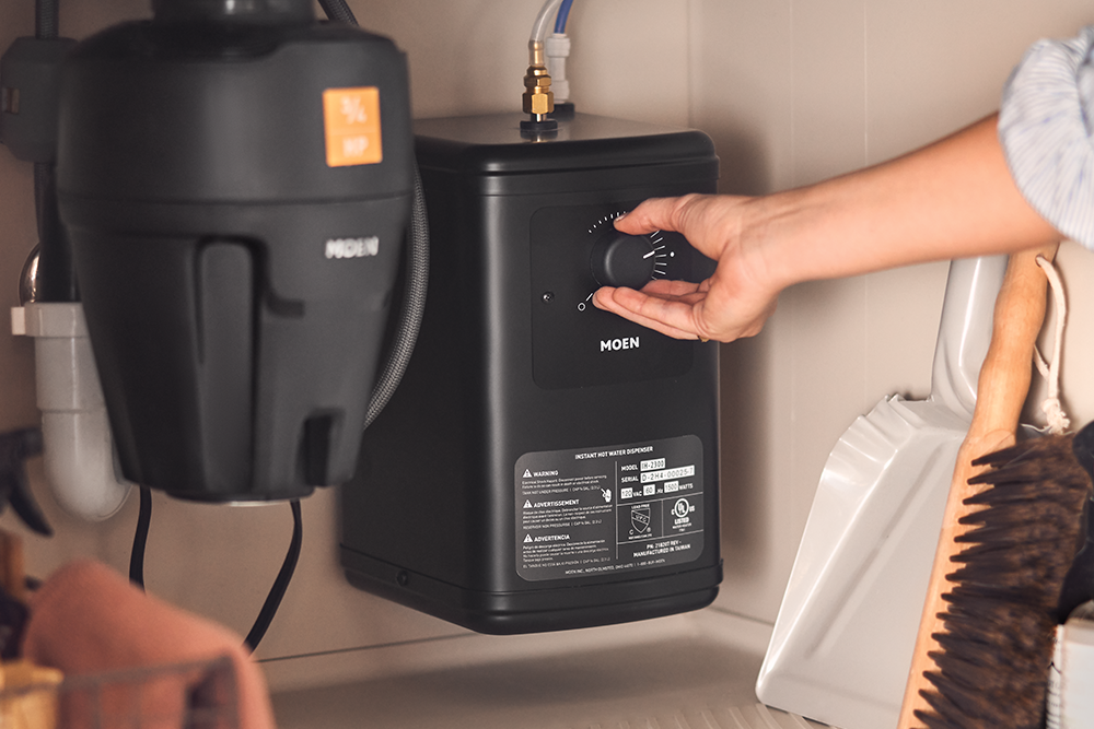 A hand adjusting the temperature on the Instant Hot tank under the sink.