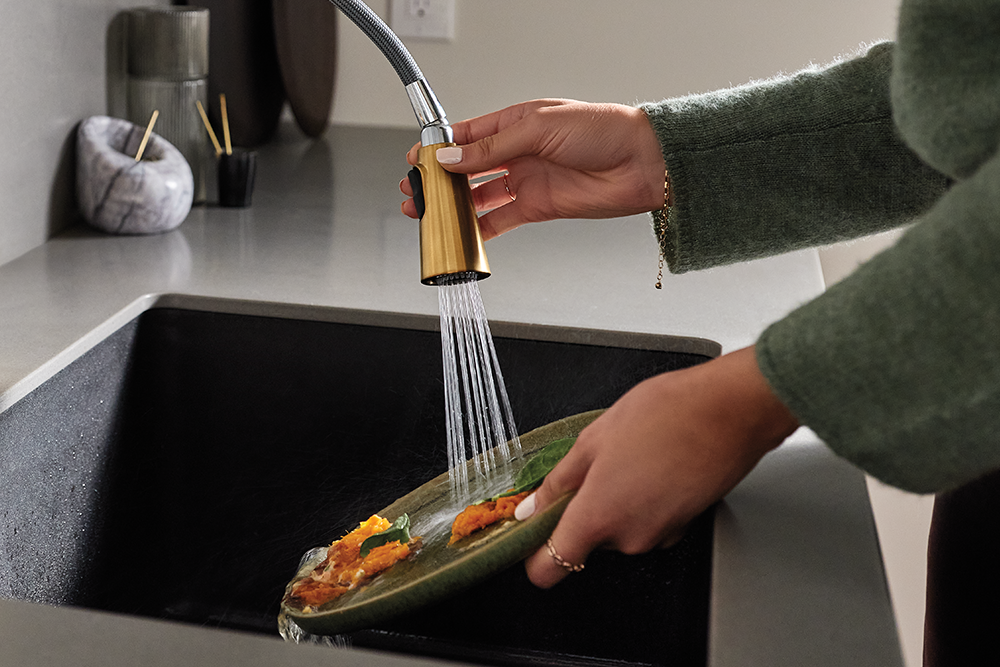 A person rinsing a plate with food remnants using a pulldown kitchen faucet.