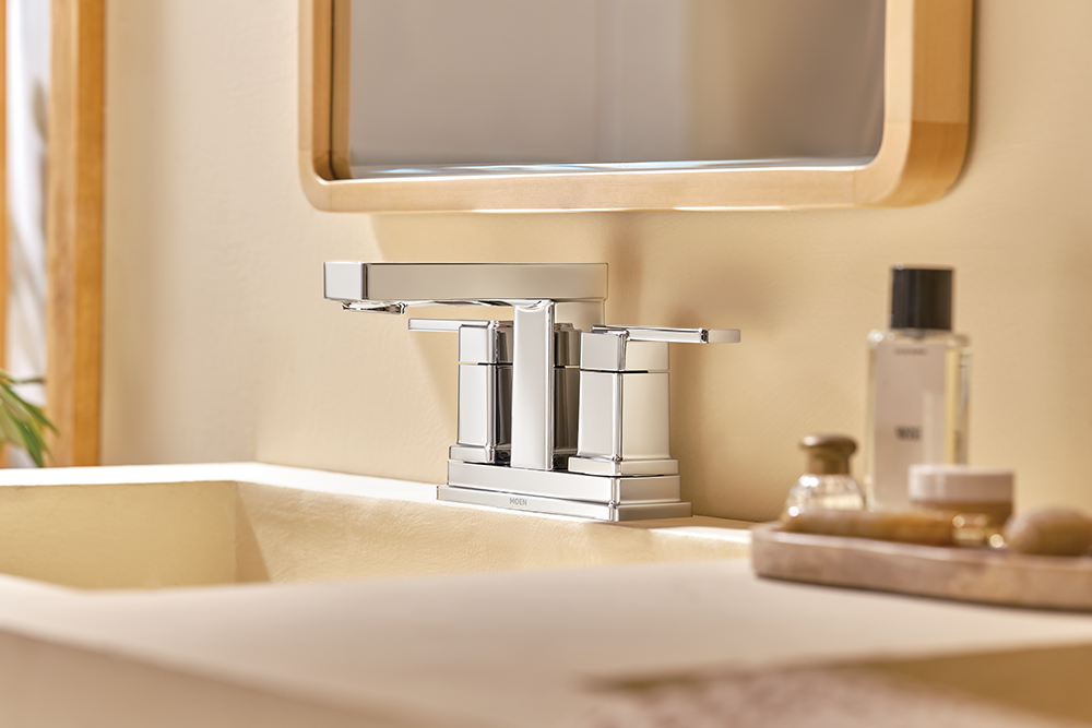 Iver Two-Handle High Arc Bathroom Faucet mounted on a beige sink, with a mirror and toiletries in the softly lit background.
