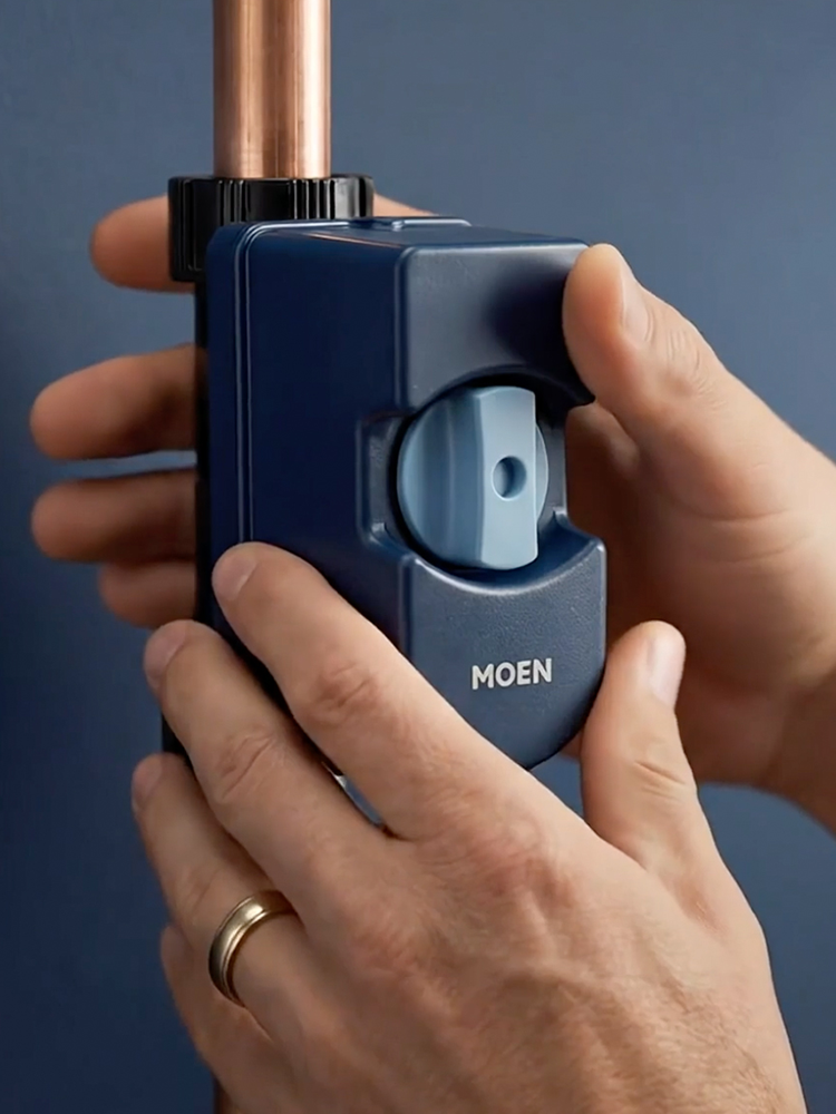 Close-up of a person's hands holding a blue MOEN water filter assembly with a copper pipe fitting above it, against a dark blue background.