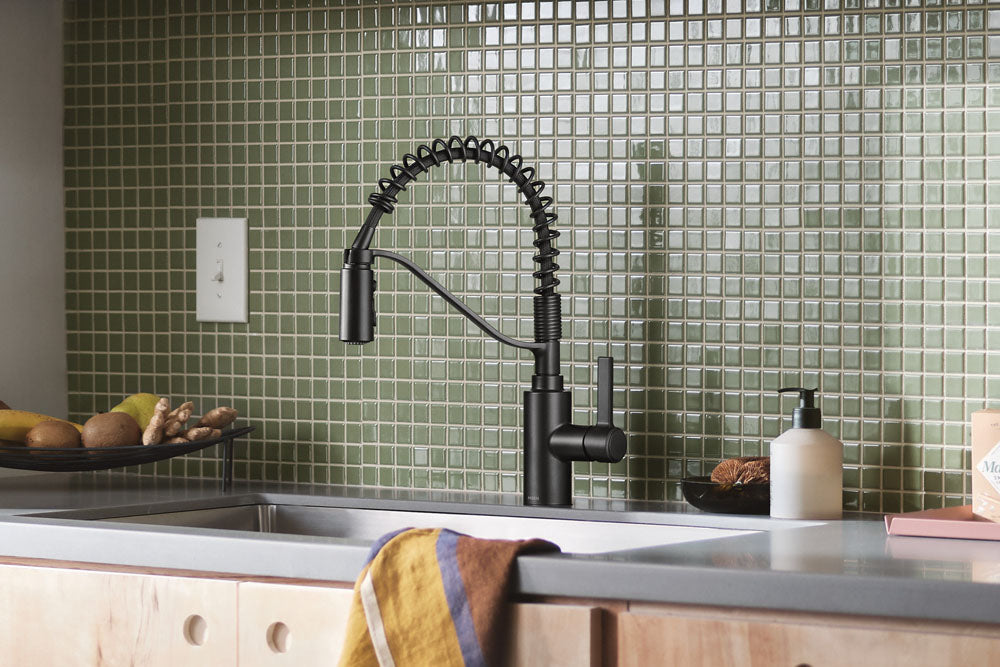 Genta LX One-Handle High Arc Pulldown Kitchen Faucet installed over a double sink, set against a green mosaic tile backsplash and light wood cabinets.