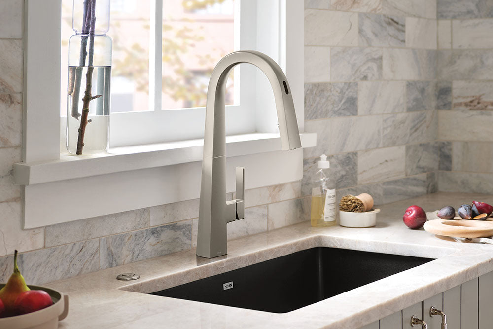 Nio One-Handle High Arc Pulldown Kitchen Faucet installed above a black undermount sink in a light marble countertop and backsplash kitchen.