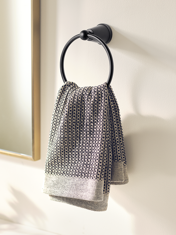 A black metal towel ring mounted on a light beige wall, holding a textured gray and black patterned kitchen towel.