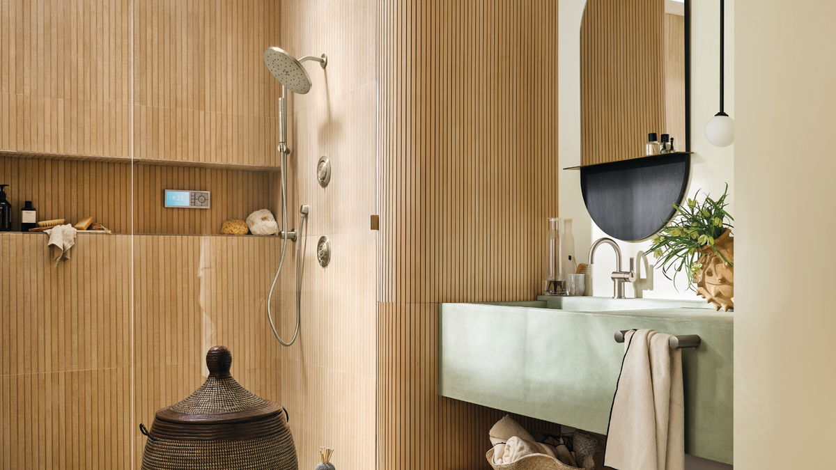 A modern bathroom interior with a wood-look slatted wall, built-in shower area, sage green vanity, mirror, sink, and hanging towel.