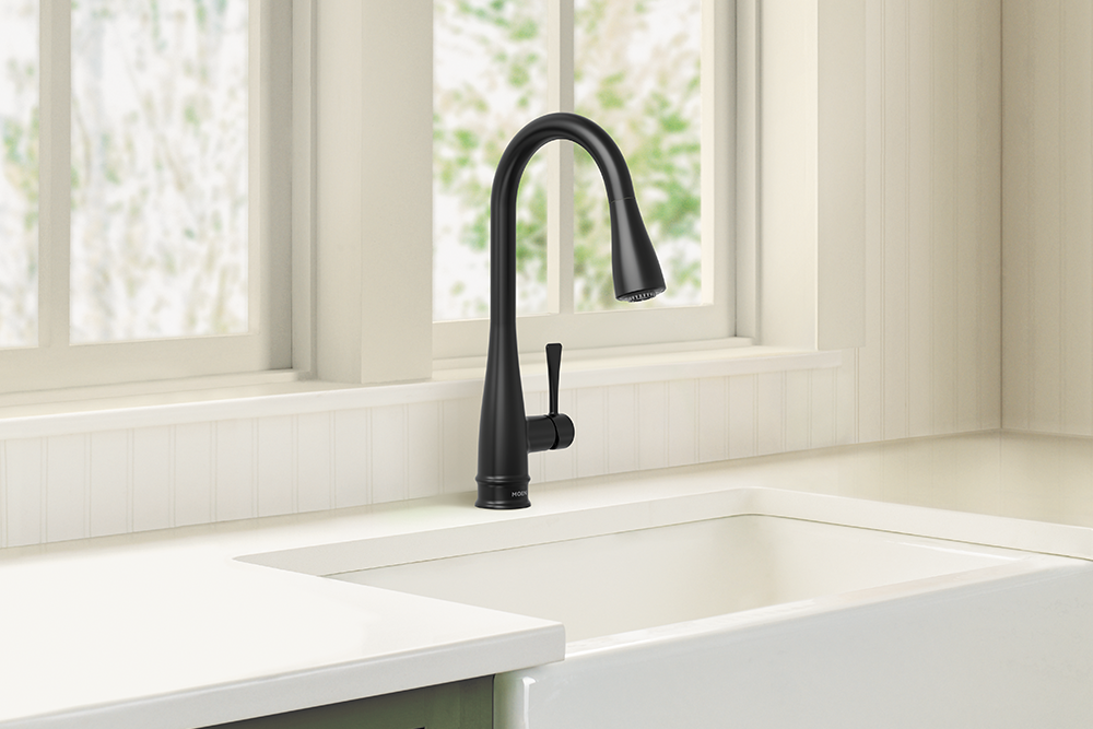 Riverwood One-Handle Kitchen Faucet, installed in a white farmhouse sink, set against a cream-colored paneled wall and window.