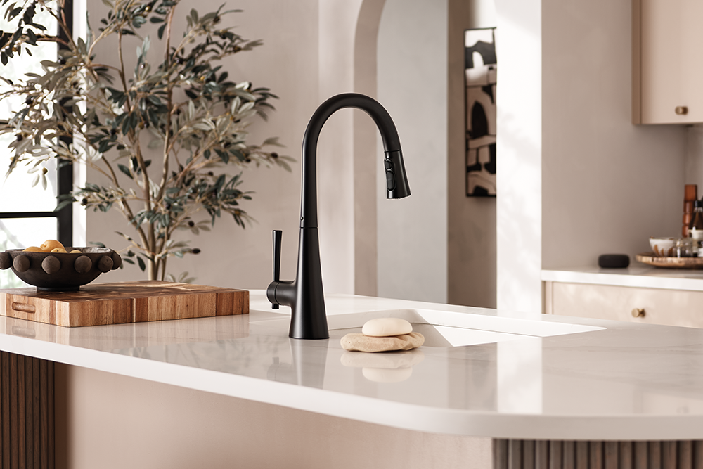 Kurv One-Handle High Arc Pulldown Kitchen Faucet, installed on a white countertop in a modern, warm-toned kitchen.