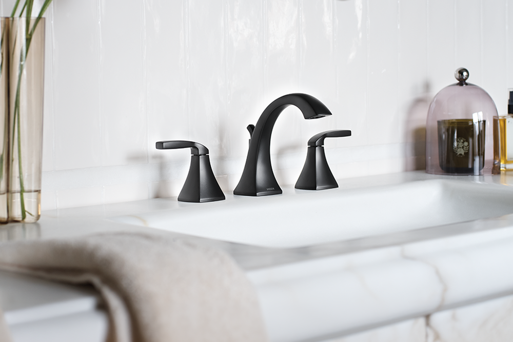 A matte black three-hole bathroom faucet set with separate hot and cold handles, installed on a white marble countertop with a white subway tile backsplash.
